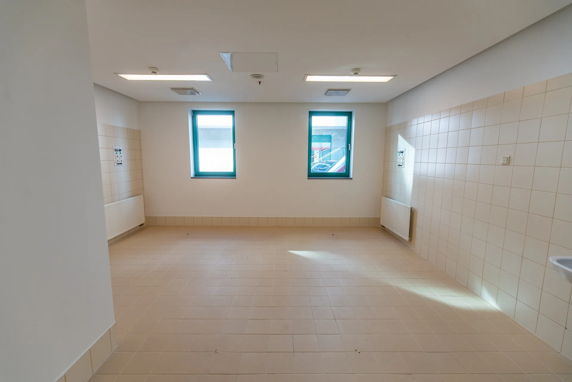 Üres, csempézett falú helyiség két ablakkal.