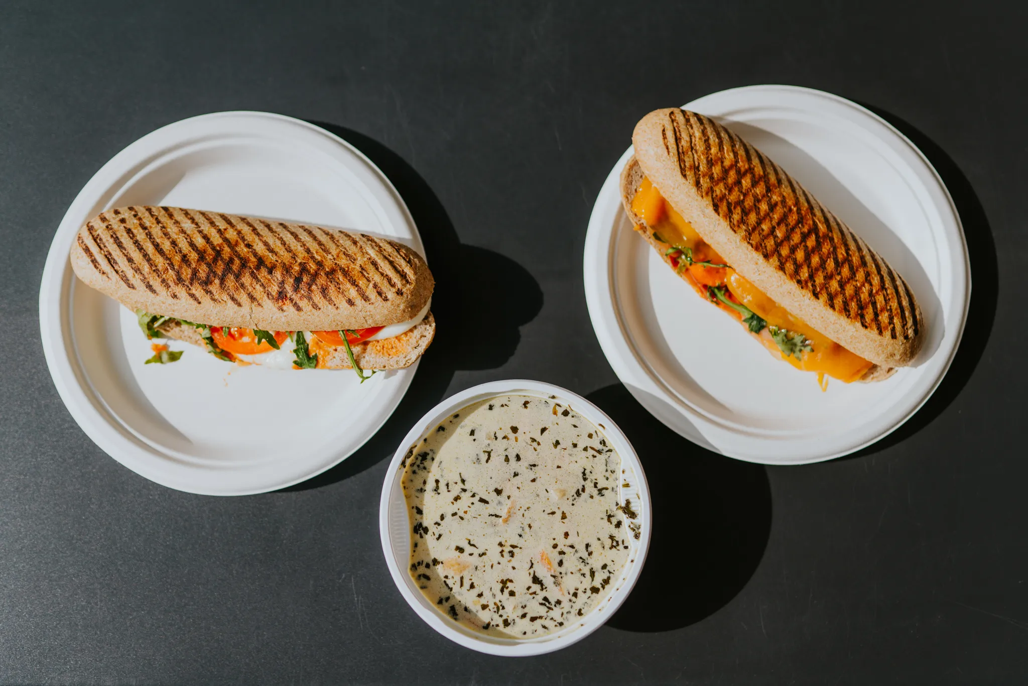 Két grillezett panini és egy tál mártogatós fekete asztalon.