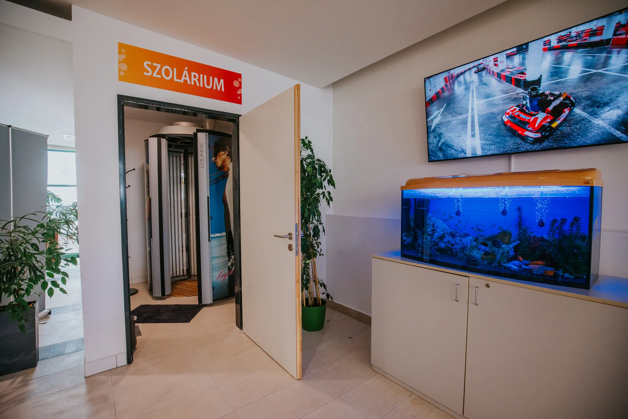 A szolárium bejárata „Szolárium” felirattal, előtte váróterem akváriummal és tévével.